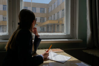 Image of a female high school student from Mongolia looking out a window with a notebook and pen