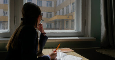 Image of a female high school student from Mongolia looking out a window with a notebook and pen