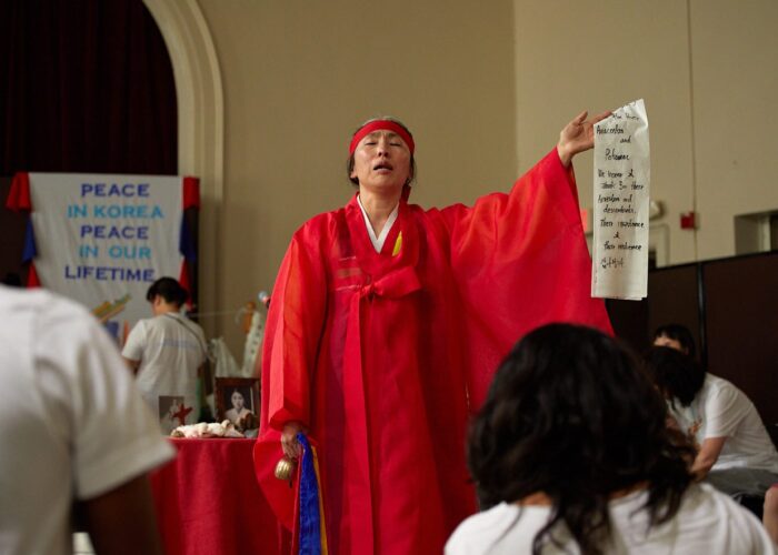 women in red Hanbok (traditional Korean clothing) holding long white paper with black writing