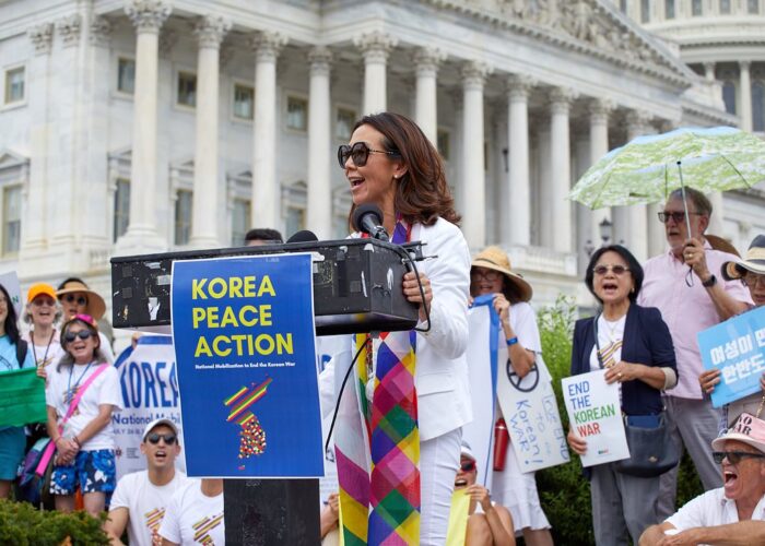 Christine Ahn speaking at podium with poster that states "Korea Peace Action"