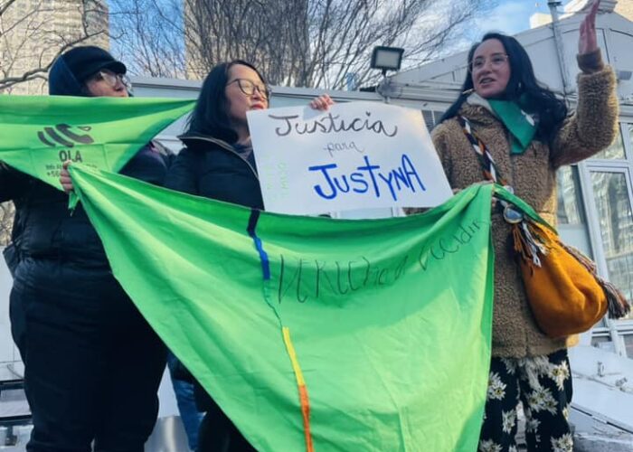 three people holding green triangles and sign that states "Justicia por Justyna"