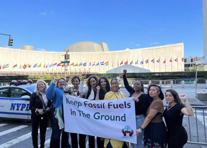 group of women posing with fisted hands above their head and with a banner that states "Keep Fossil Fuels in The Ground"