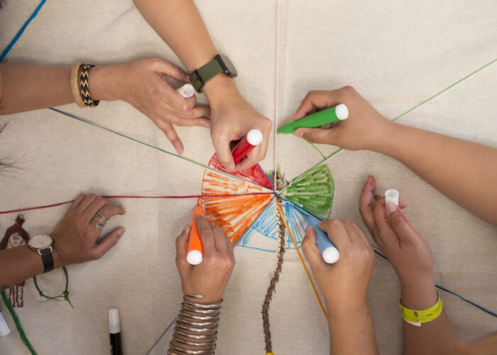 Hands of women working together to color a piece of indigenous art