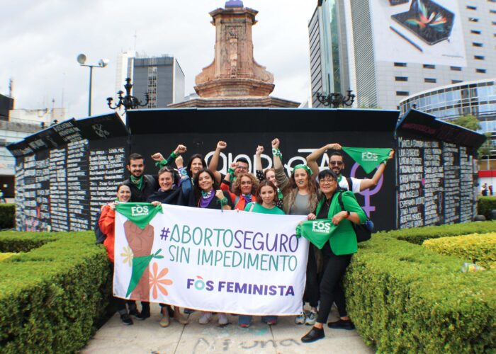 Fos Feminista community with fists above their heads in front of a banner with the Spanish hashtag AboritoSeguroSinImpedimento (in English roughly translates to Safe Abortion Without Impediment)