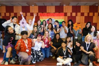Workshop attendees stand in front of Pride flag