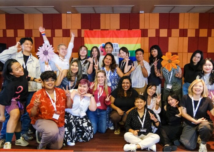 Workshop attendees stand in front of Pride flag