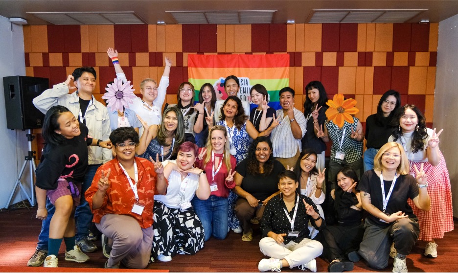Workshop attendees stand in front of Pride flag