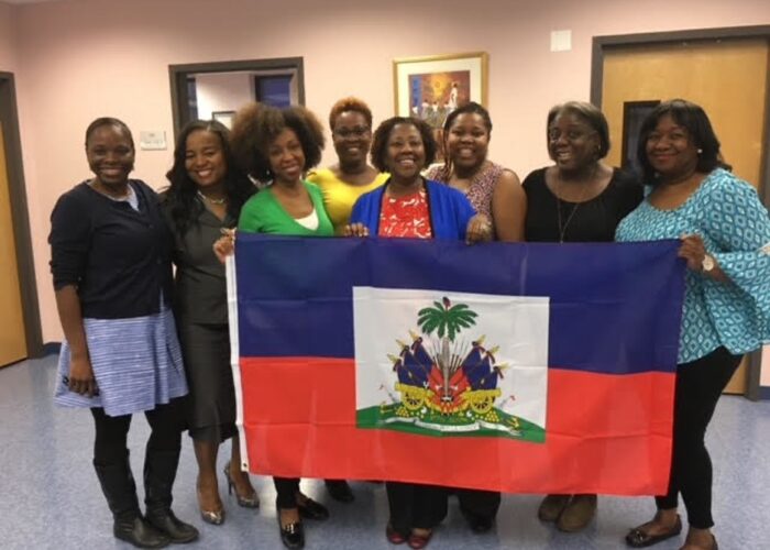 Group of smiling women hold up flag of Haiti