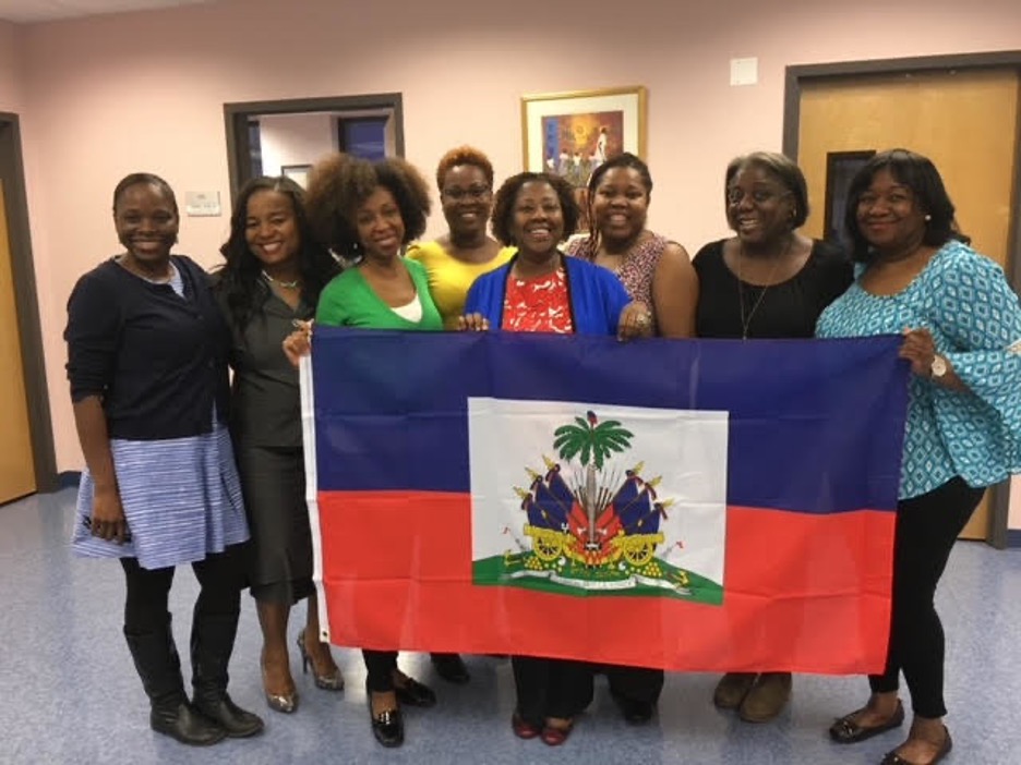 Group of smiling women hold up flag of Haiti